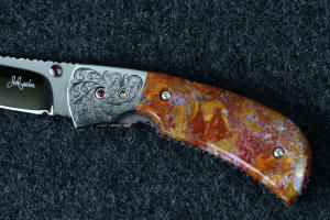 "Bellatrix" custom folding knife, obverse side view showing maker's mark, engraving detail, faceted garnets set in stainless steel, engraved screw fasteners